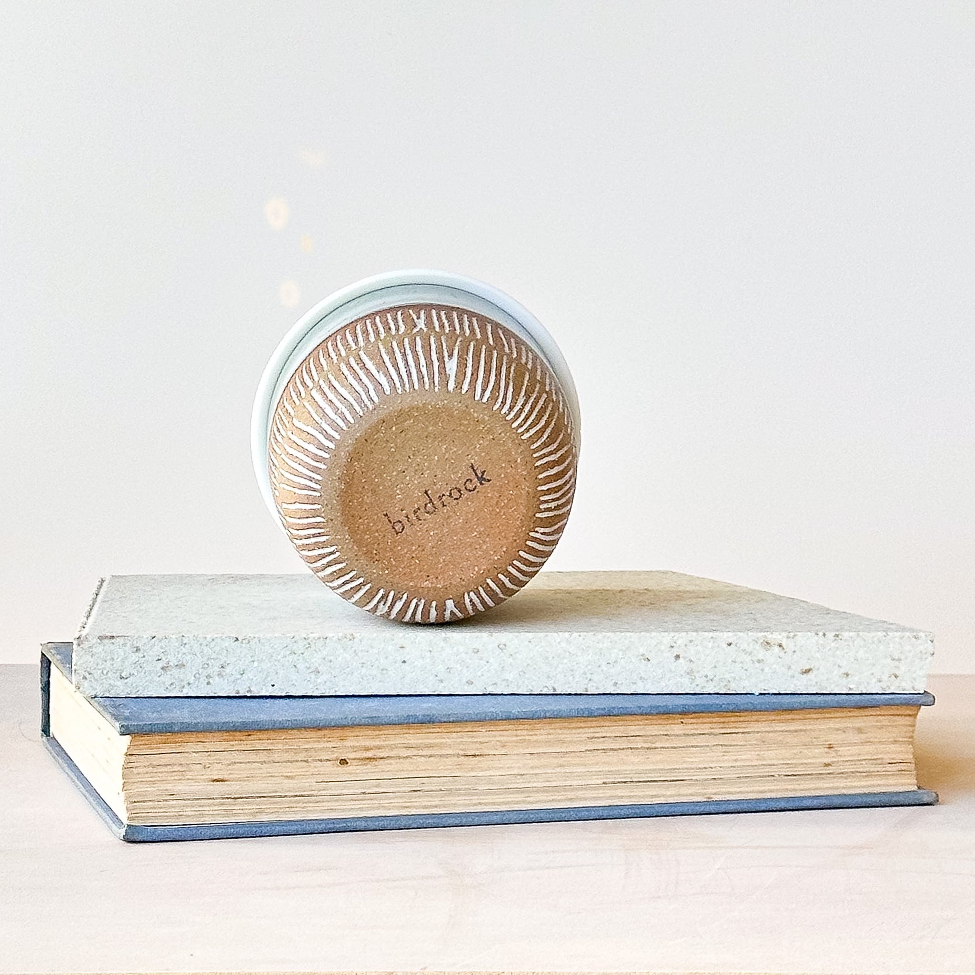 Base view of a ceramic keep cup on top of a stack of books with a light background