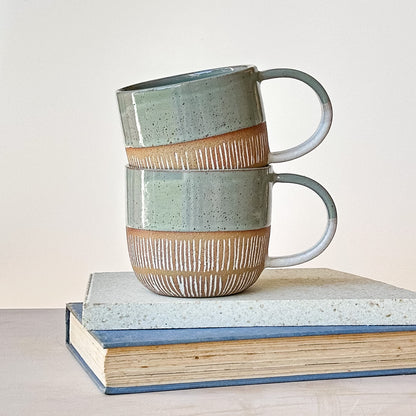 Two ceramic mugs stacked on a book with a plain background