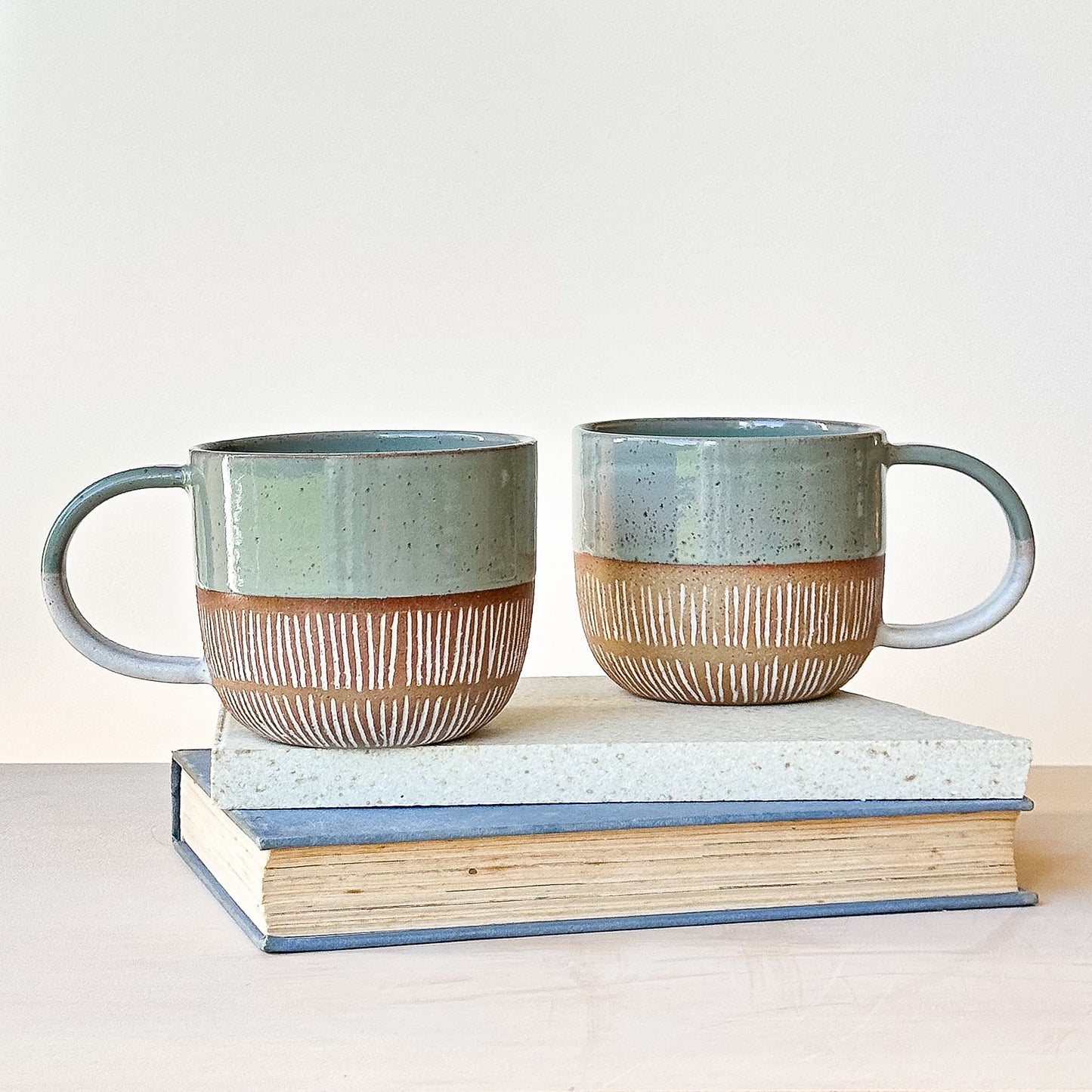 Two ceramic mugs with striped design on a stack of books against a light background