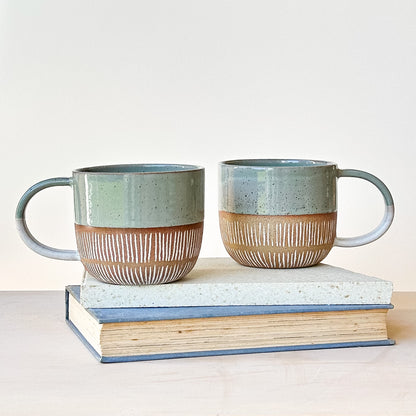 Two ceramic mugs with striped design on a stack of books against a light background