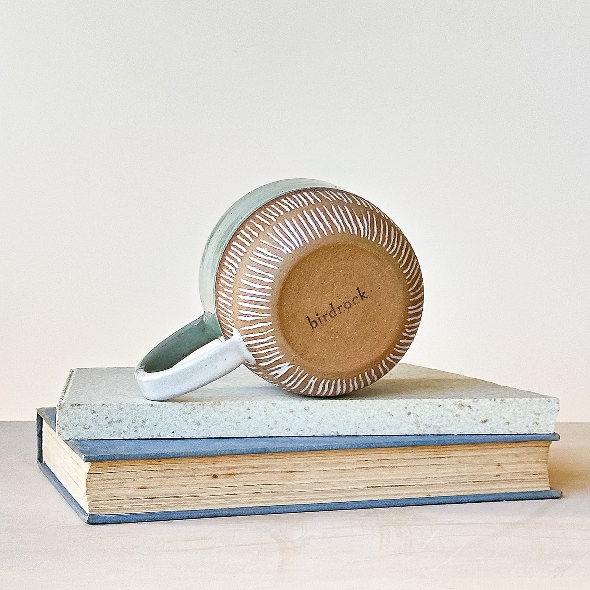 Ceramic mug with textured design on a stack of books, featuring the brand 'birdrock'.