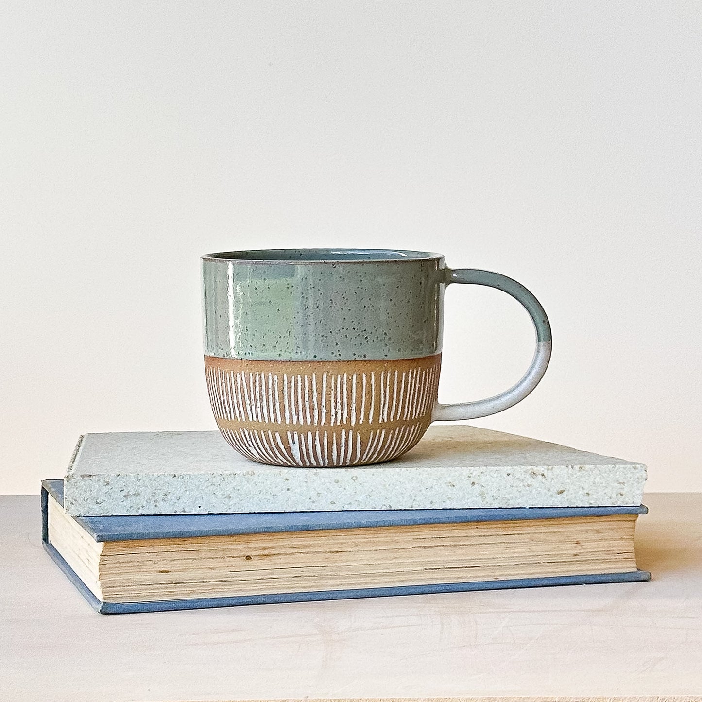 Ceramic mug with a textured design on top of two books against a light background