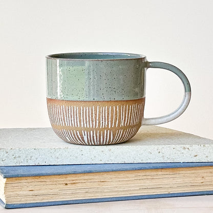 Ceramic mug with a textured design on top of books against a light background