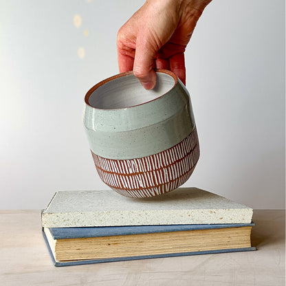Ceramic planter pot with striped design being held above two stacked books on a light surface.