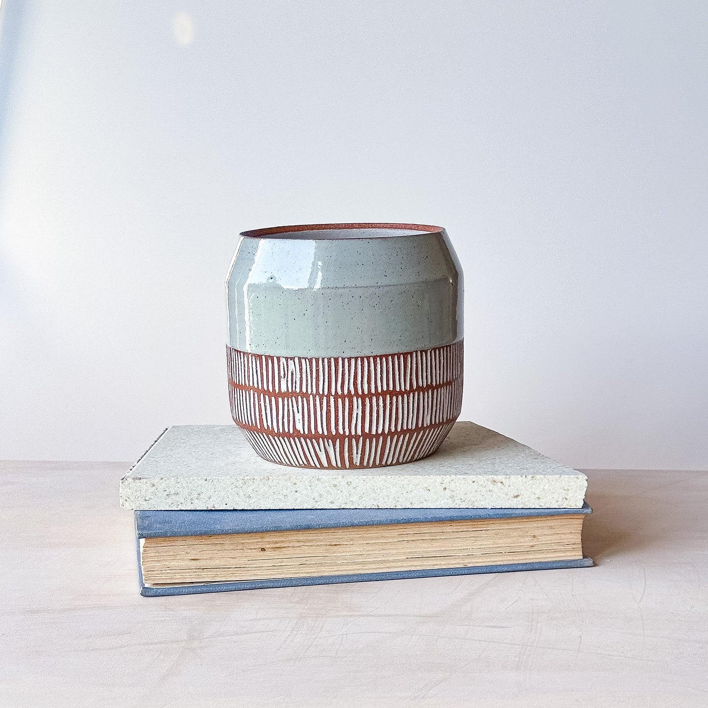 Ceramic pot with striped design on top of a book against a white background