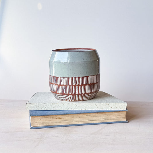Ceramic pot with striped design on top of a book against a white background