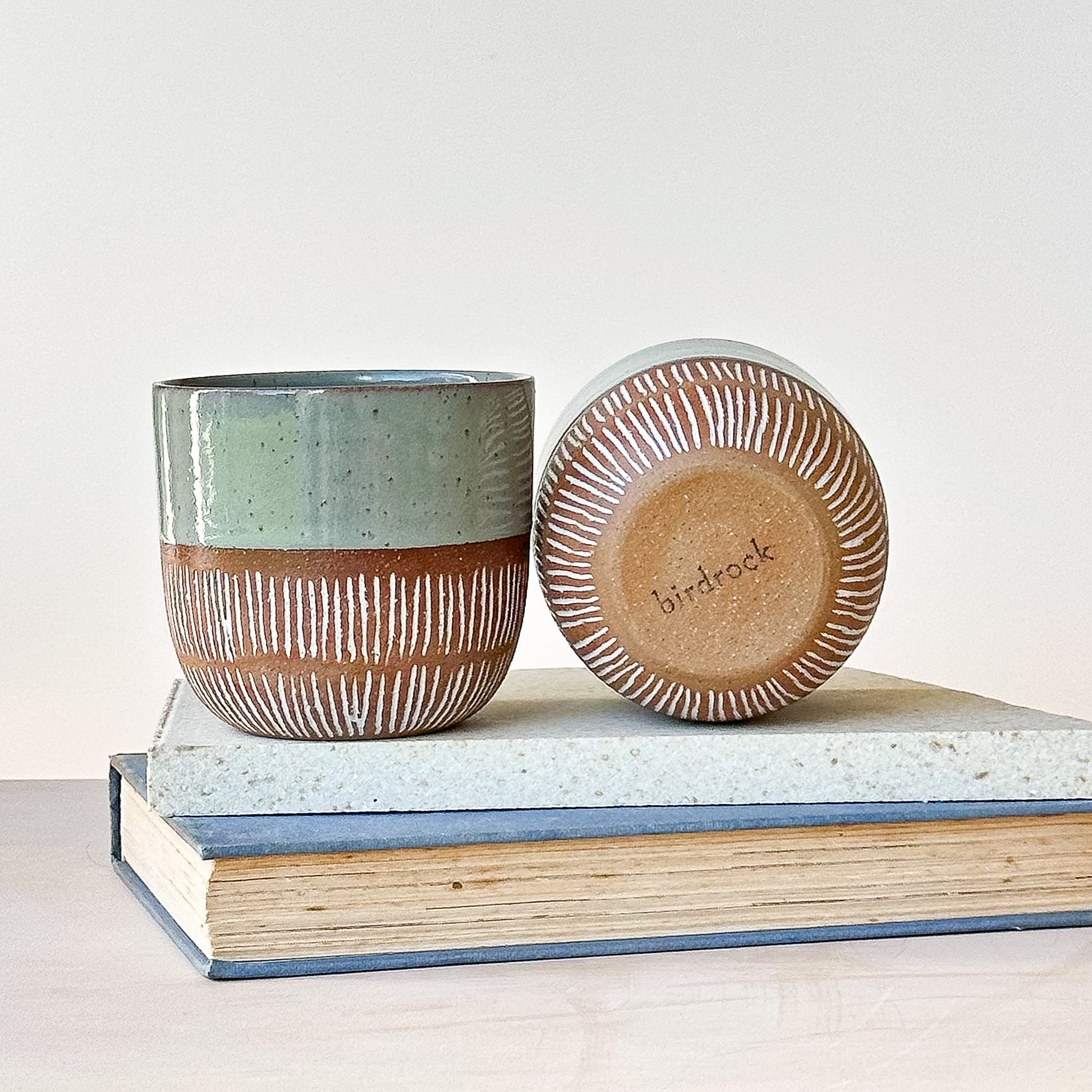 Ceramic container with a lid on top of books, featuring the brand 'birdrock' on the lid.