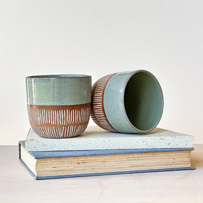 Two ceramic pots with textured surfaces on top of a book against a light background