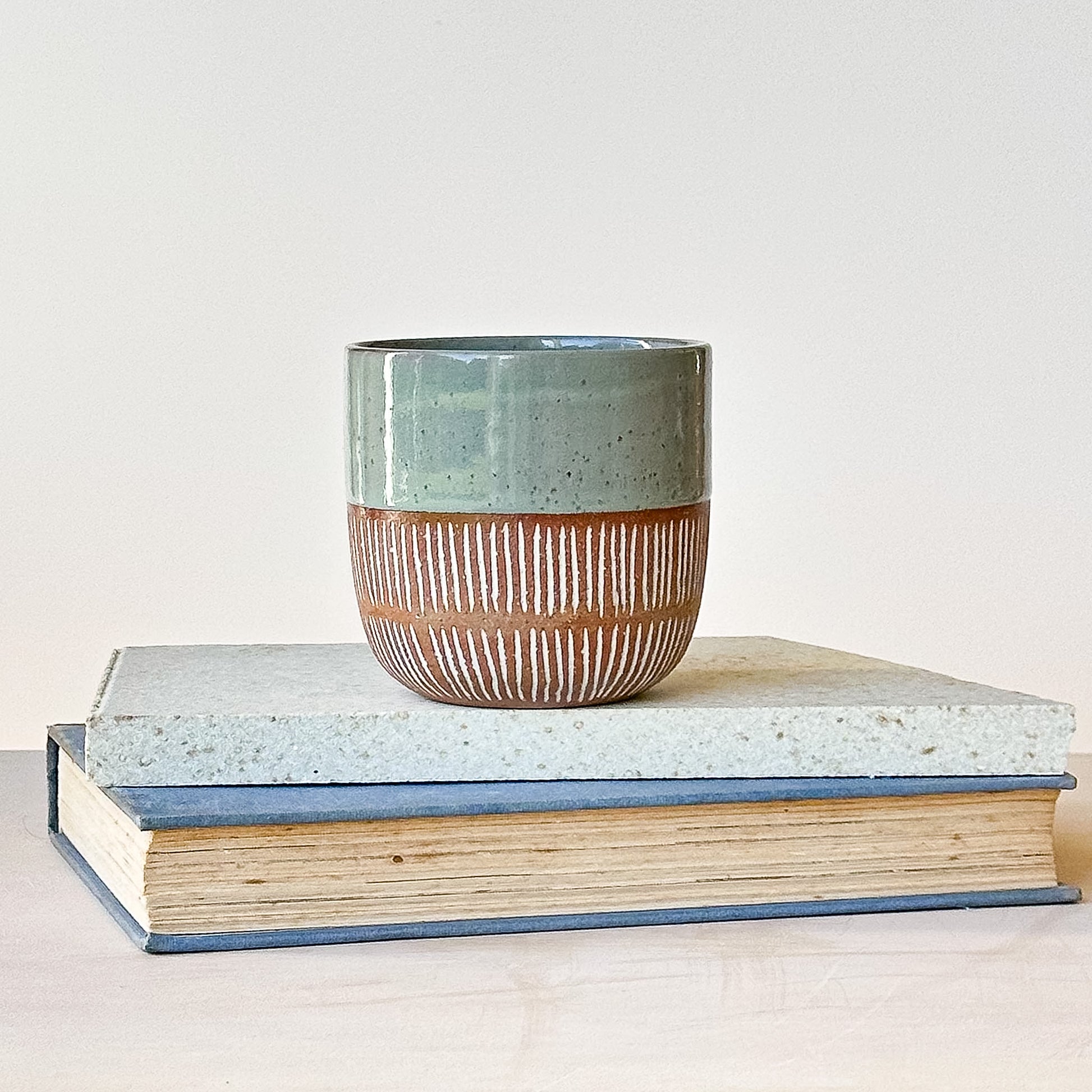Ceramic cup with textured design on top of two books against a light background