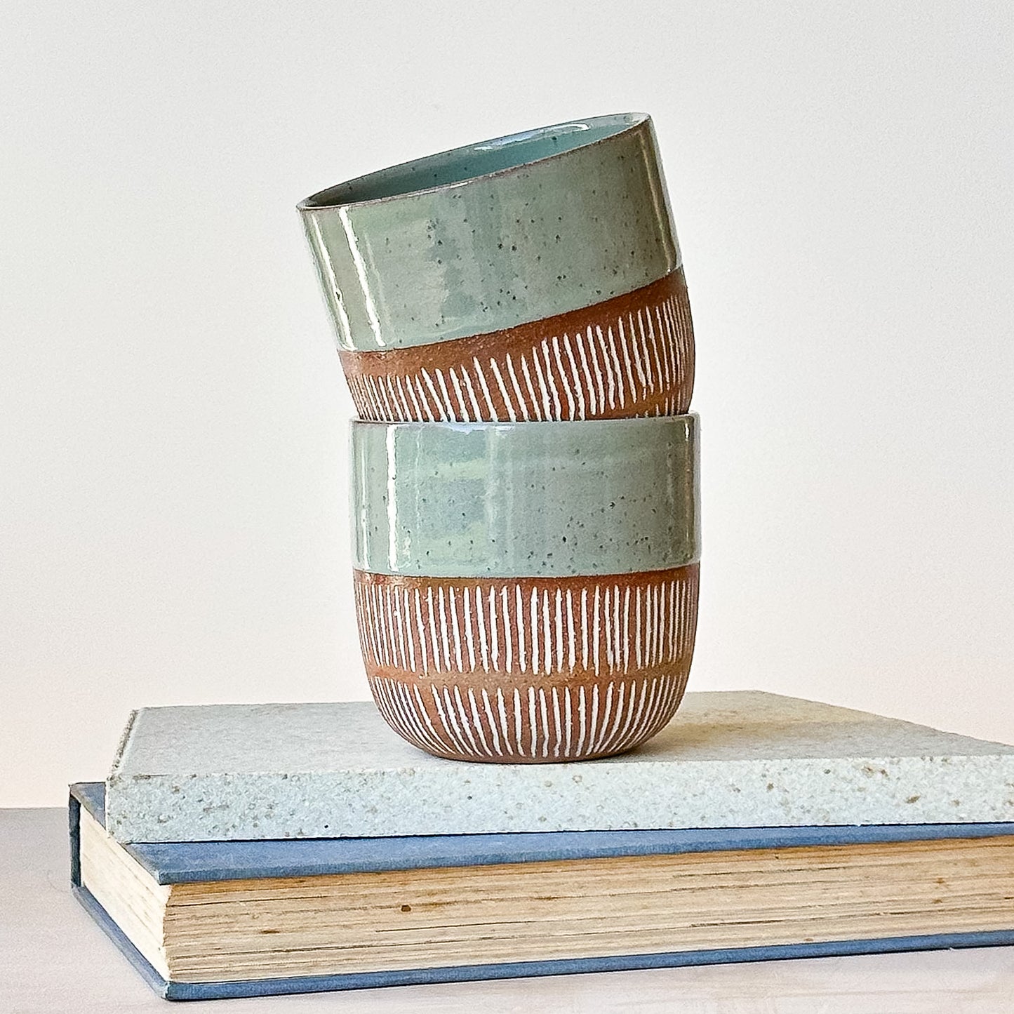 Two ceramic cups with striped design stacked on top of each other on a book.