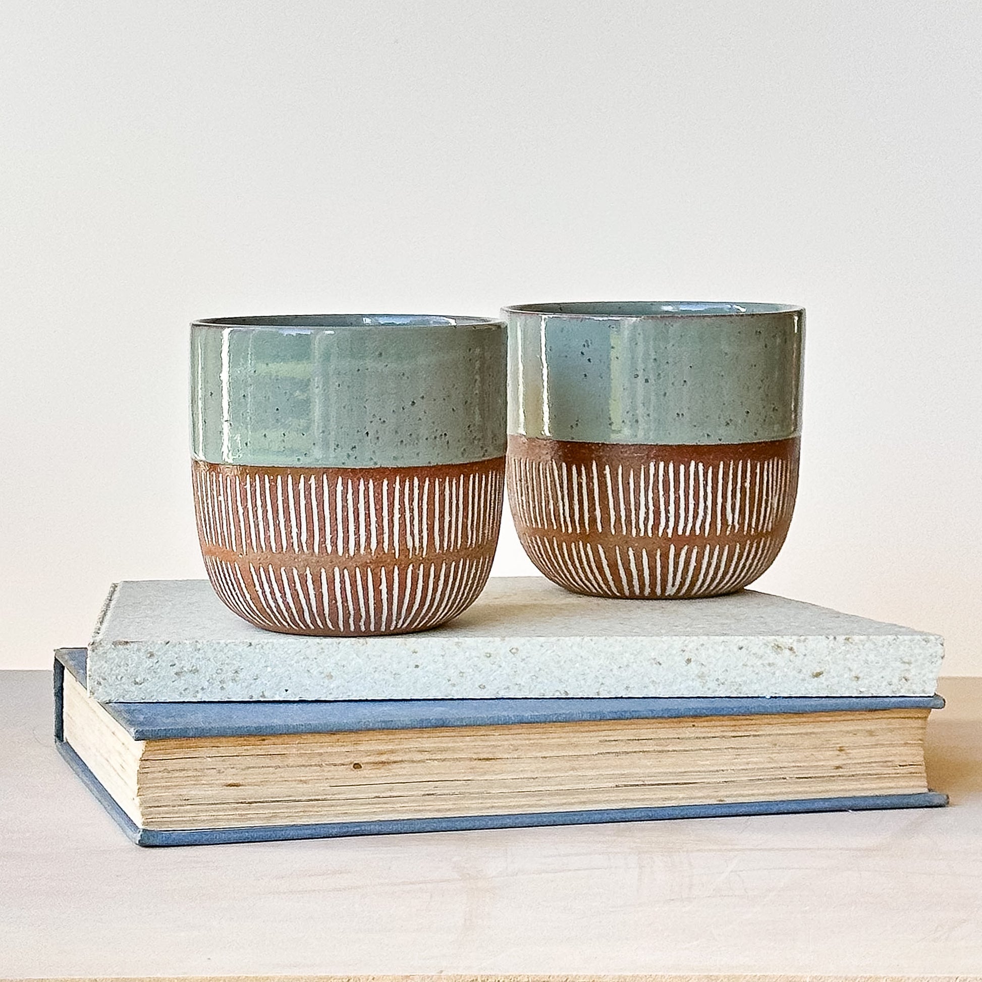 Two ceramic pots with a textured finish on top of a book against a light background