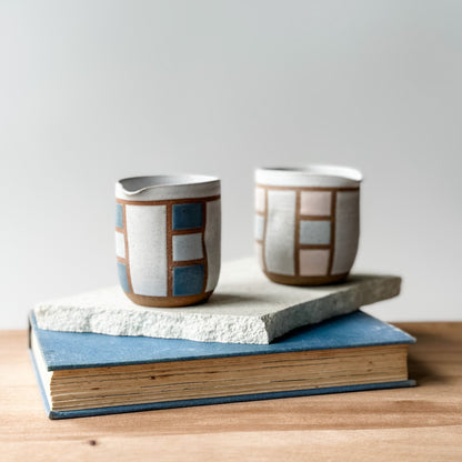 Two ceramic cups with geometric patterns on a stack of books against a light background