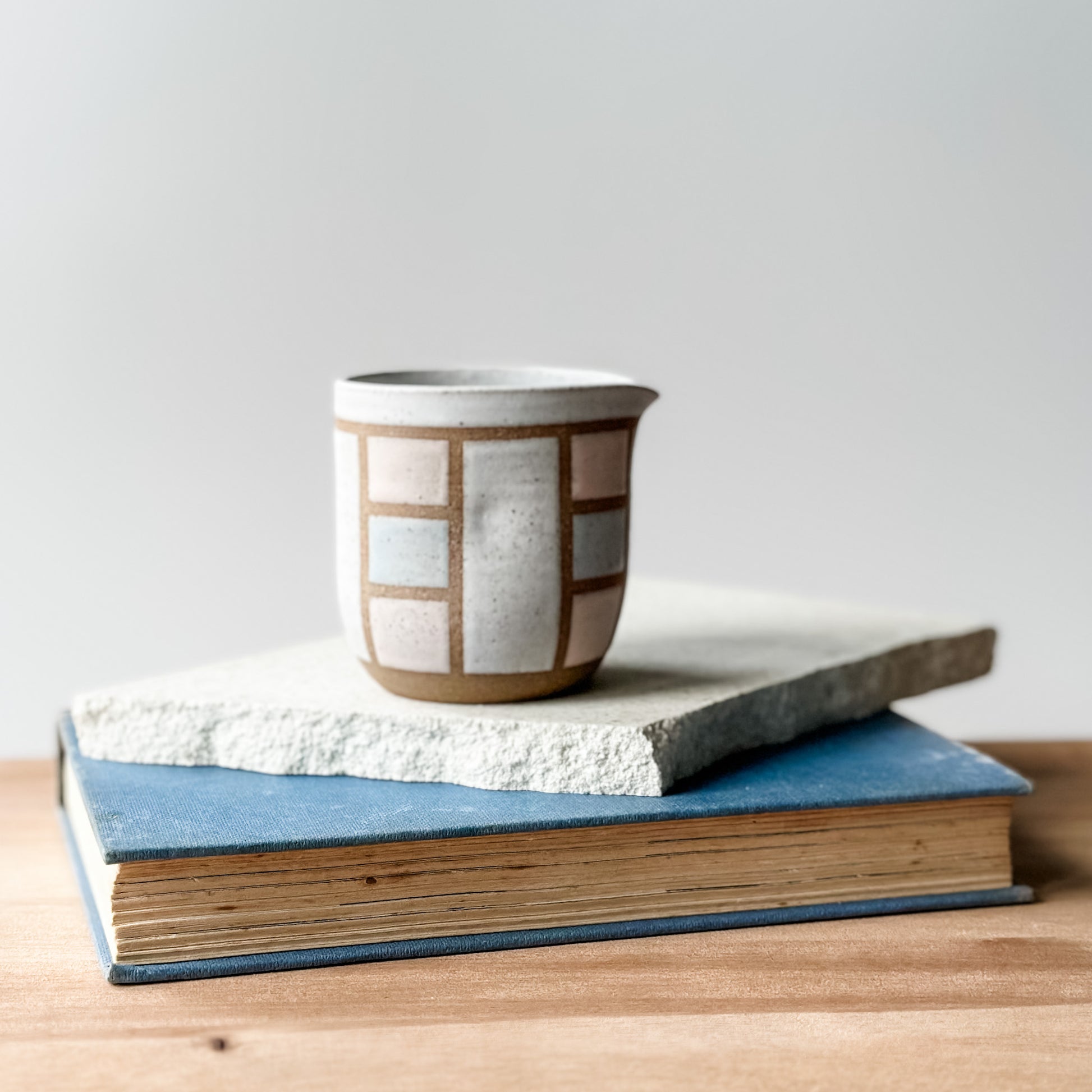 A creamer jug with a geometric pattern on a tile and a book.