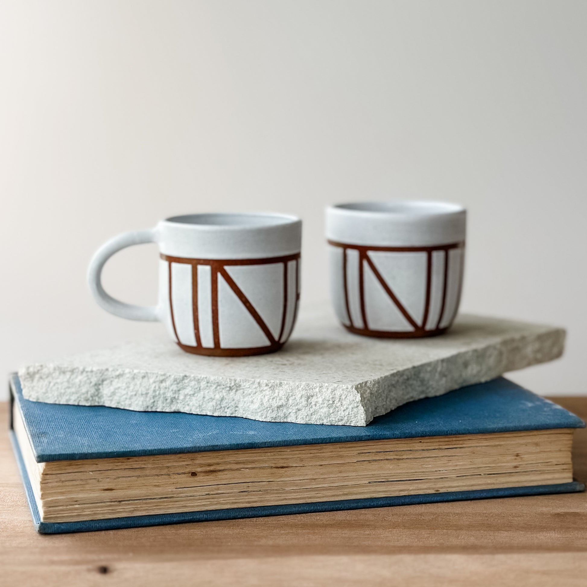 Two ceramic mugs with geometric design on a stack of books.