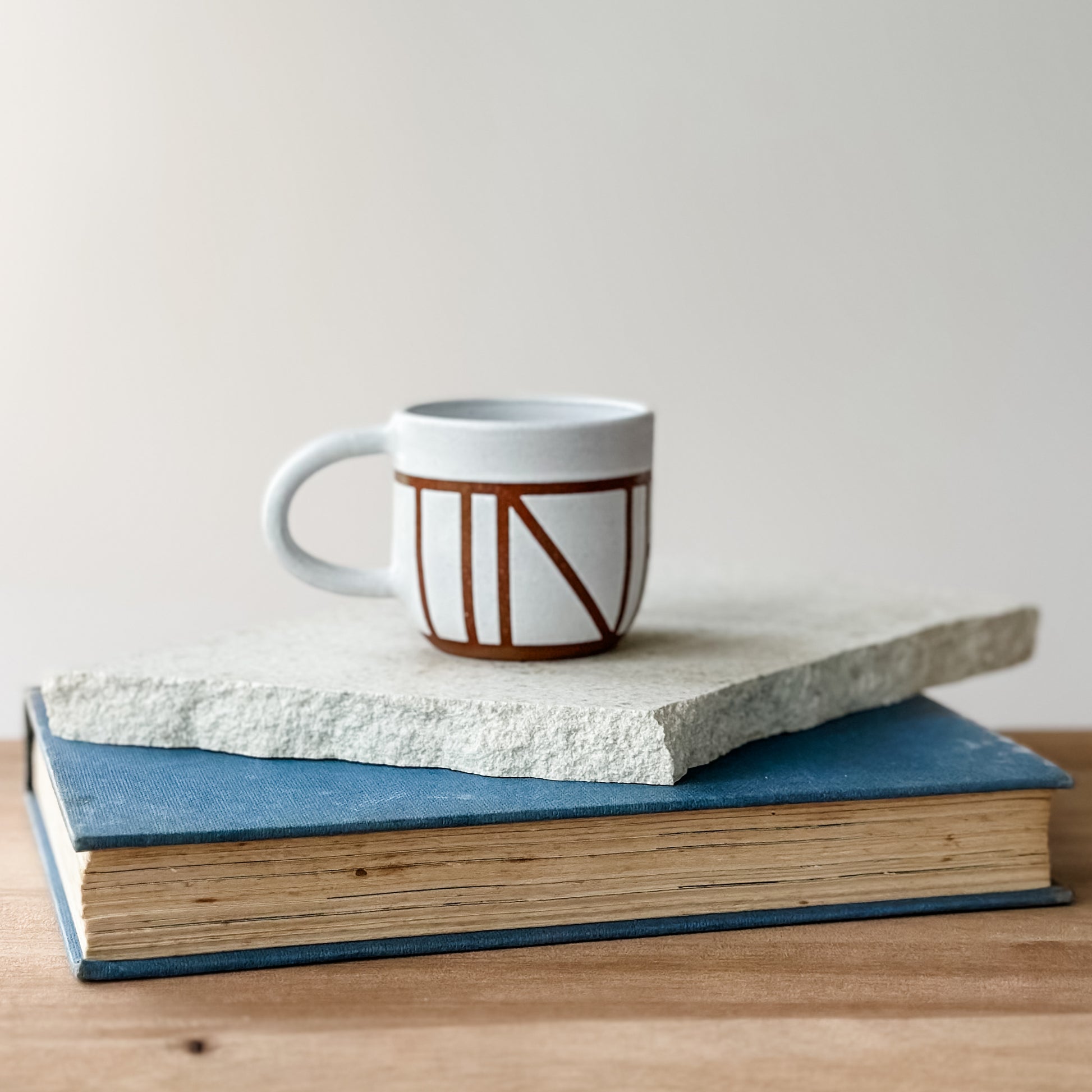 Ceramic mug with geometric design on top of a stack of books on a wooden surface.