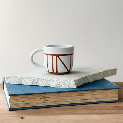 Ceramic mug with geometric design on top of a stack of books on a wooden surface.