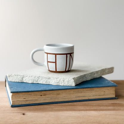 Ceramic mug with geometric design on top of two books on a wooden surface.