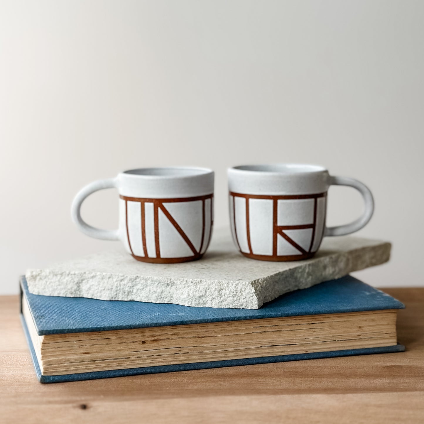 Two ceramic mugs with geometric design on a stack of books