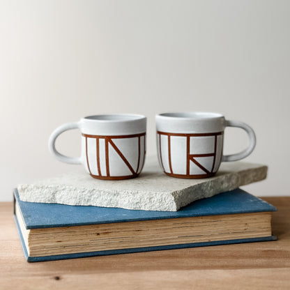 Two ceramic mugs with geometric design on a stack of books