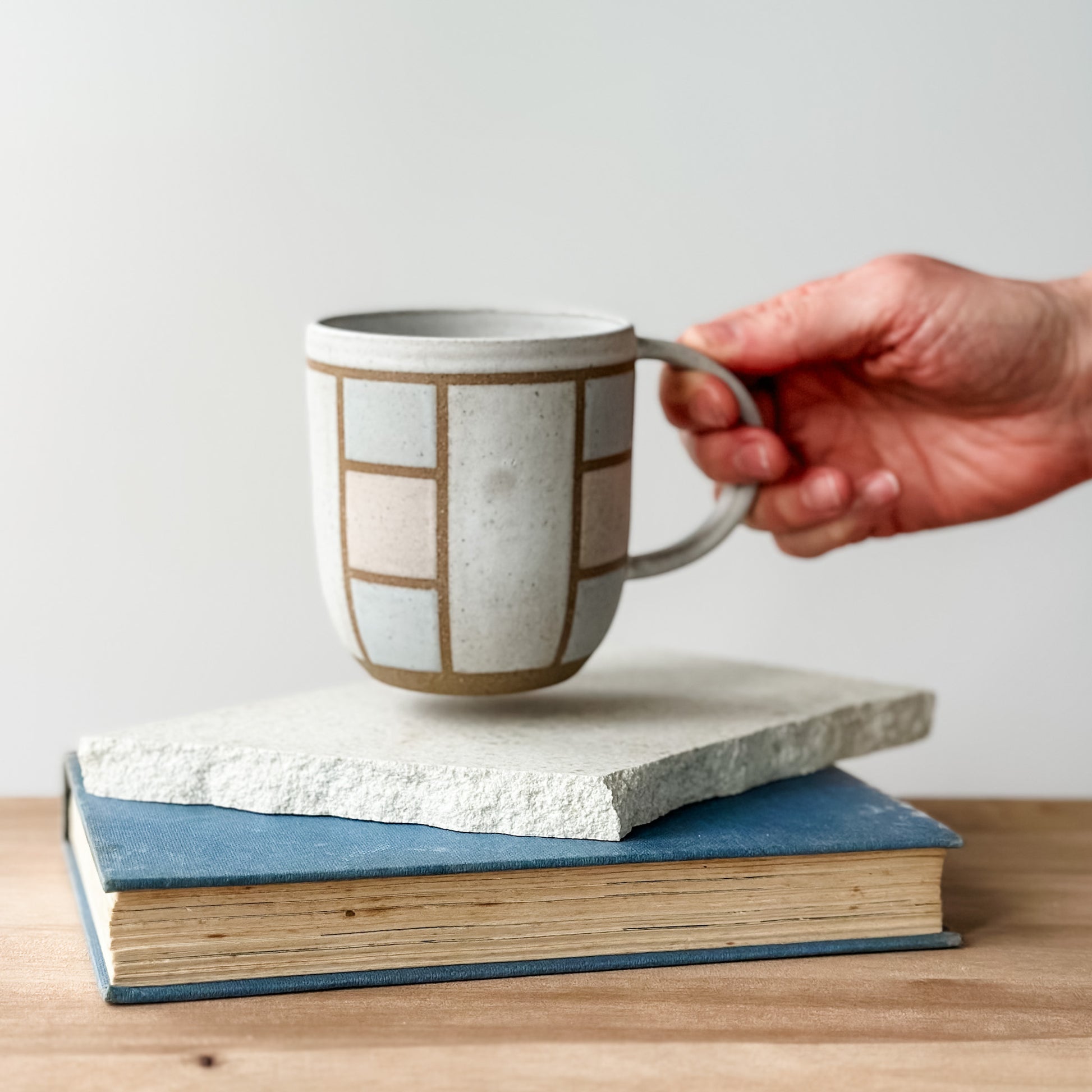 Hand holding a ceramic mug on top of two books with a plain background