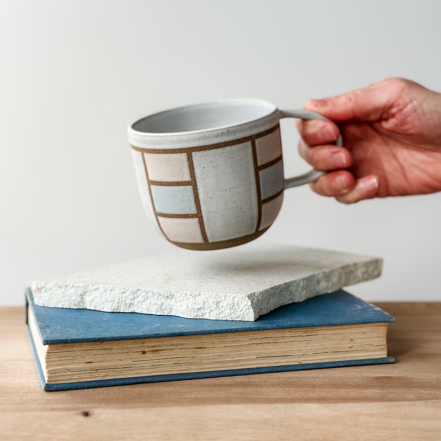 Hand holding a ceramic mug with geometric design on top of two books.