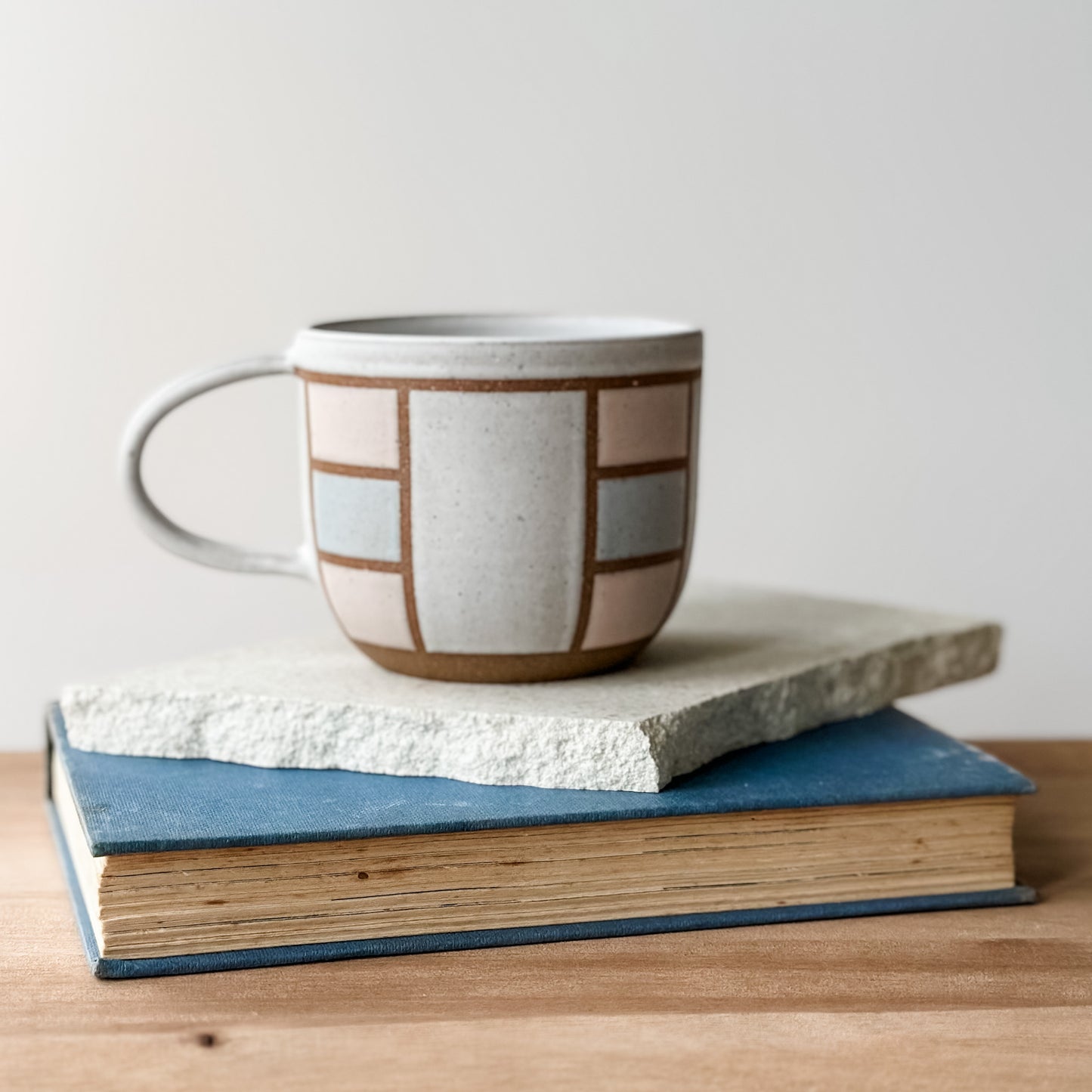 Ceramic mug with geometric pattern on top of two books on a wooden surface.