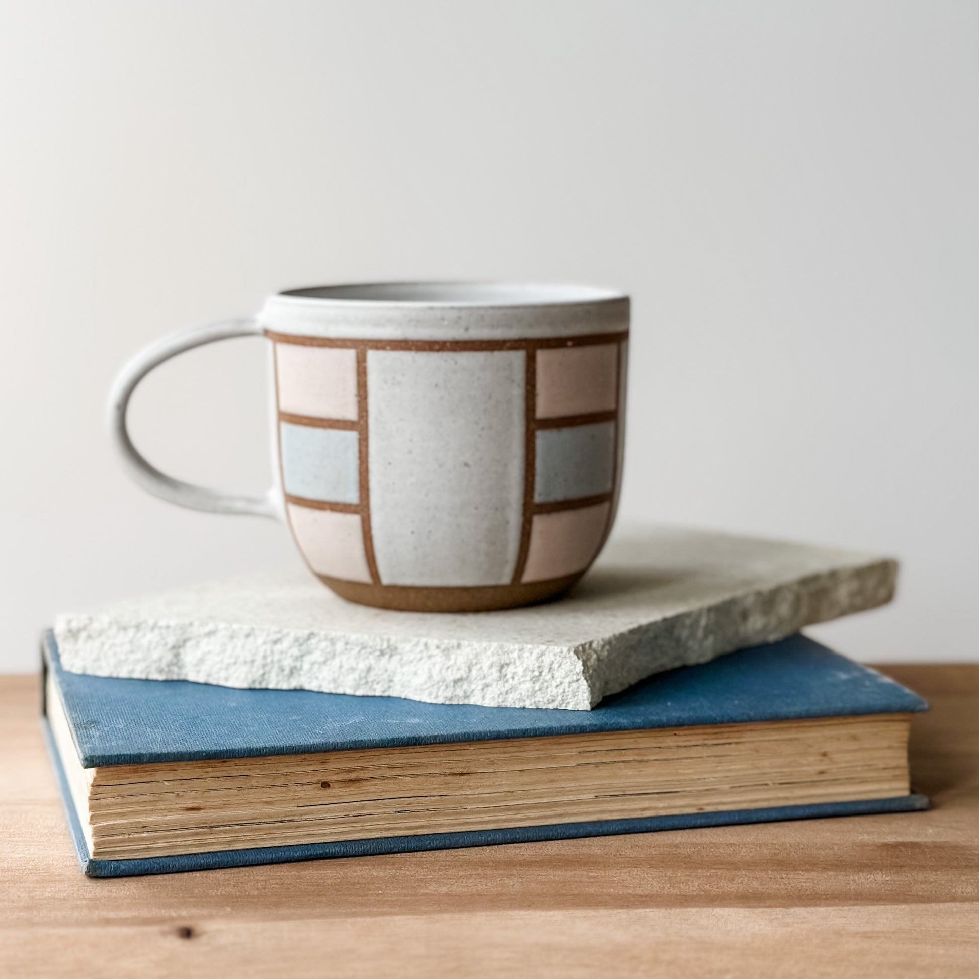 Ceramic mug with geometric pattern on top of two books on a wooden surface.