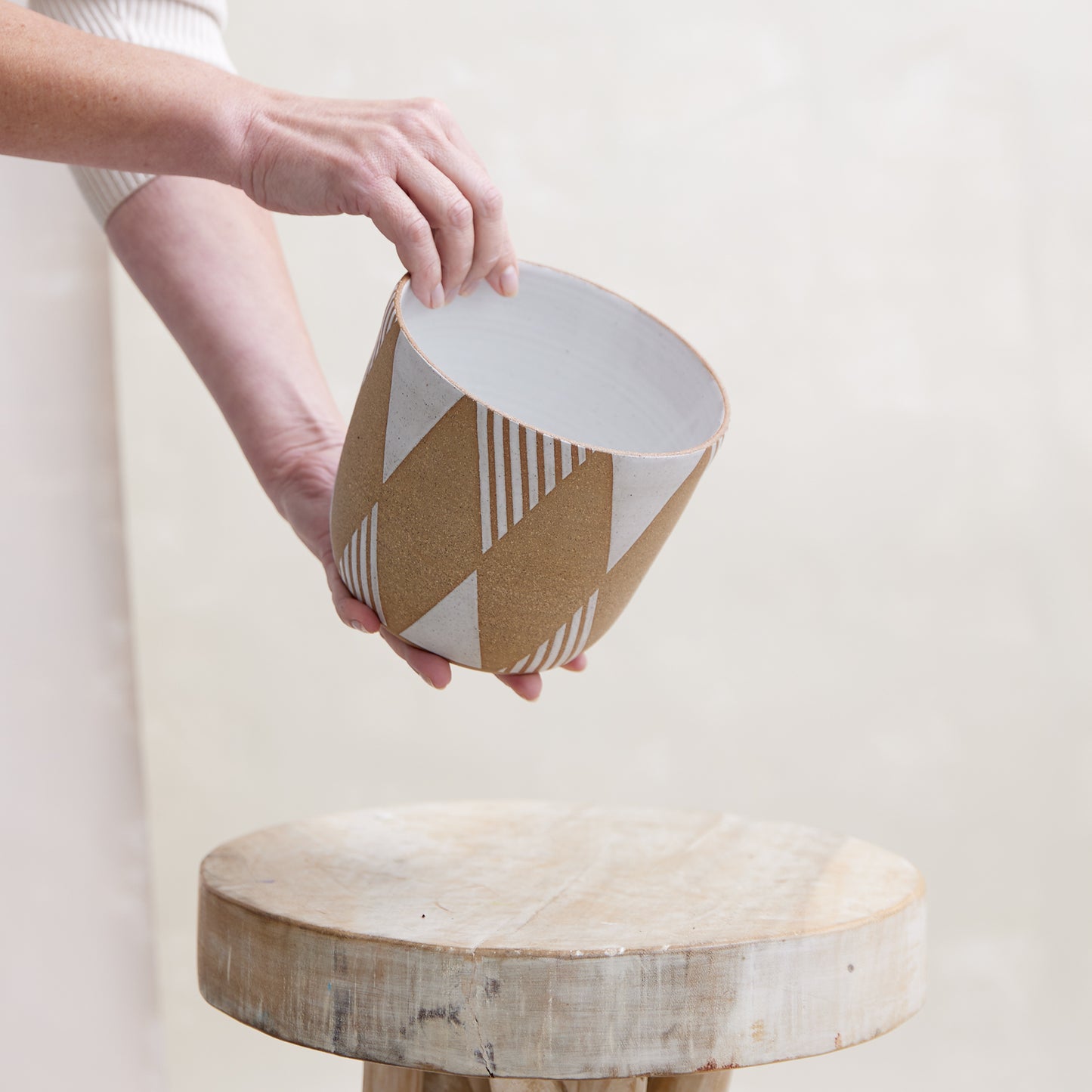 A front view of the Geometric Handmade Ceramic Planter Pot in a white glaze. The handmade planter is placed by hand atop a wooden stool in a coastal-styled setting.