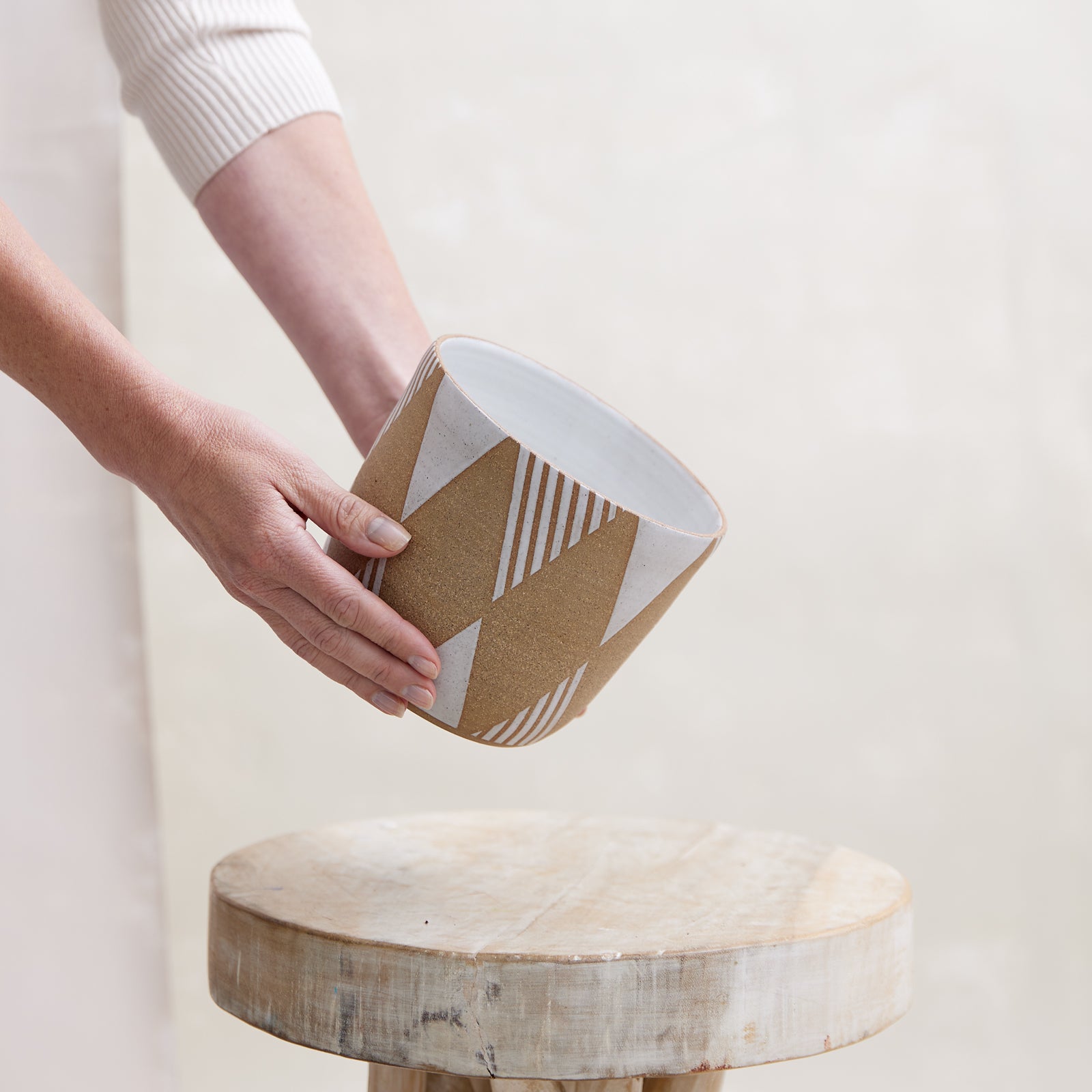 A front view of the Geometric Handmade Ceramic Planter Pot in a white glaze. The handmade planter is placed by hand atop a wooden stool in a coastal-styled setting.