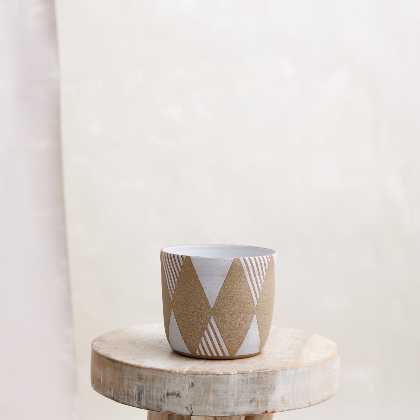 A front view of the Geometric Handmade Ceramic Planter Pot in a white glaze. The handmade planter sits atop a wooden stool in a coastal-styled setting.