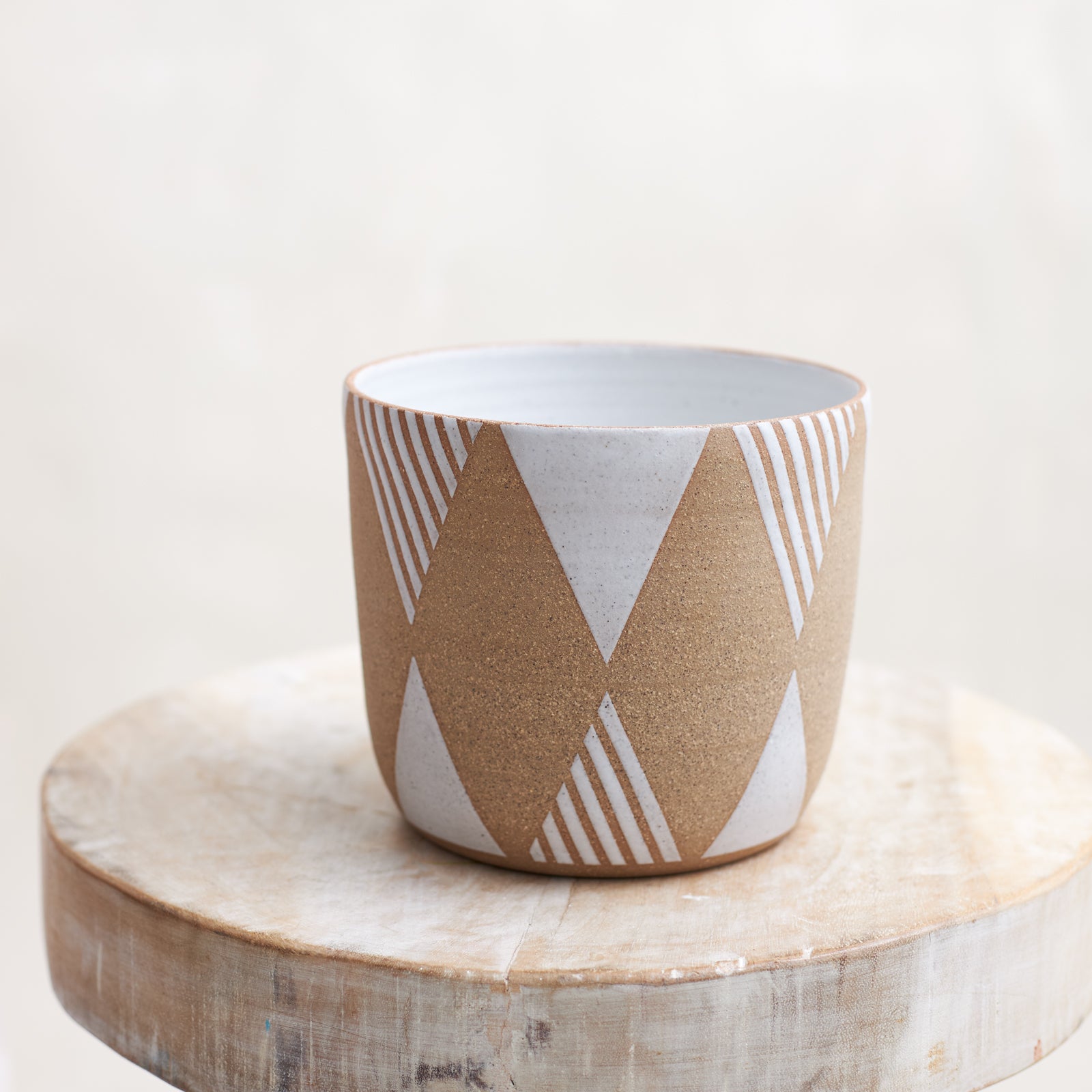 A front view of the Geometric Handmade Ceramic Planter Pot in a white glaze. The handmade planter sits atop a wooden stool in a coastal-styled setting.