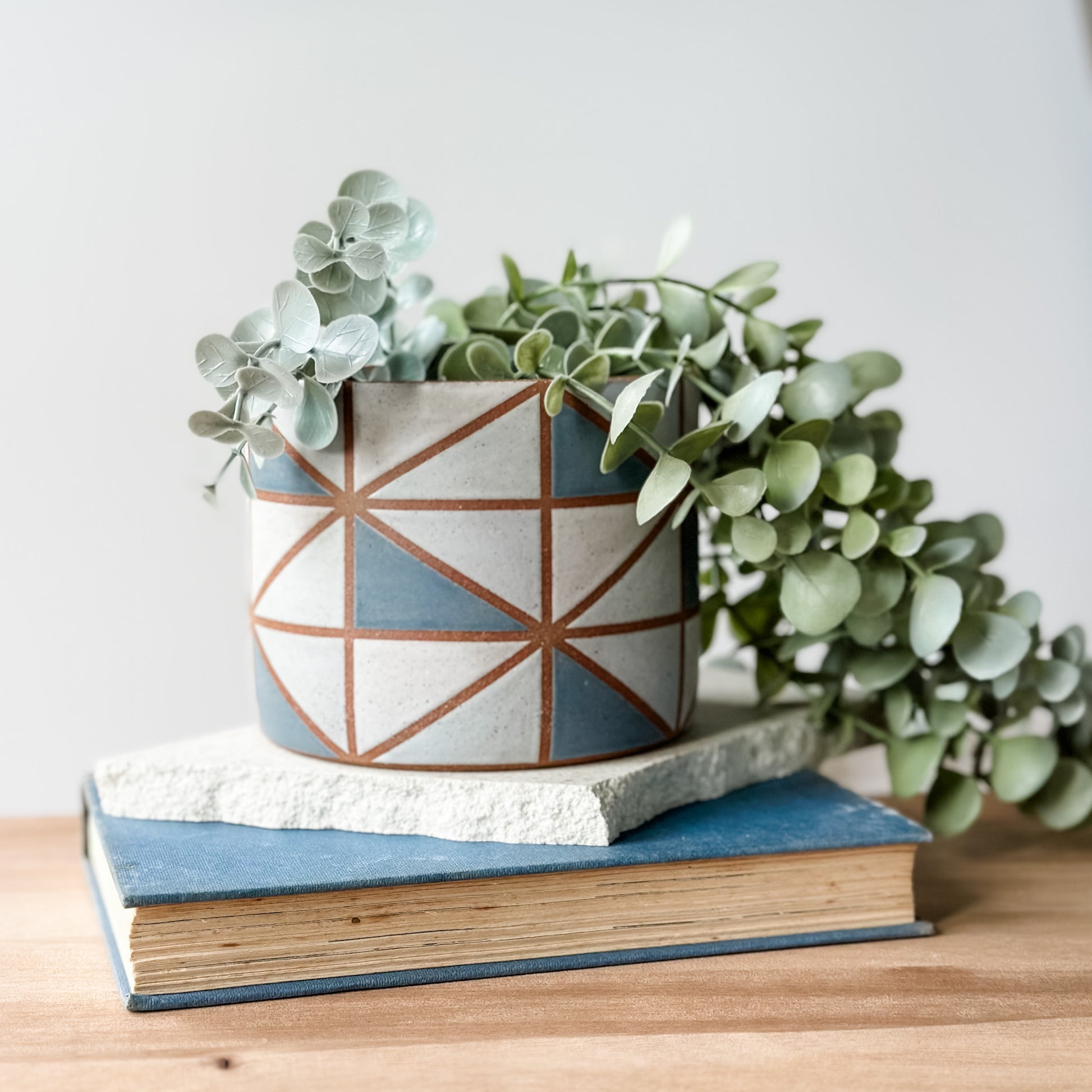 Ceramic planter with geometric design on top of a book, featuring a small plant.