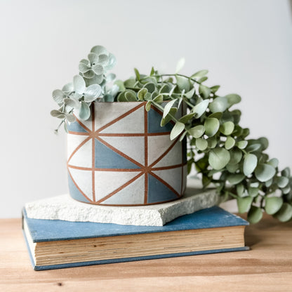 Ceramic planter with geometric design on top of a book, featuring a small plant.
