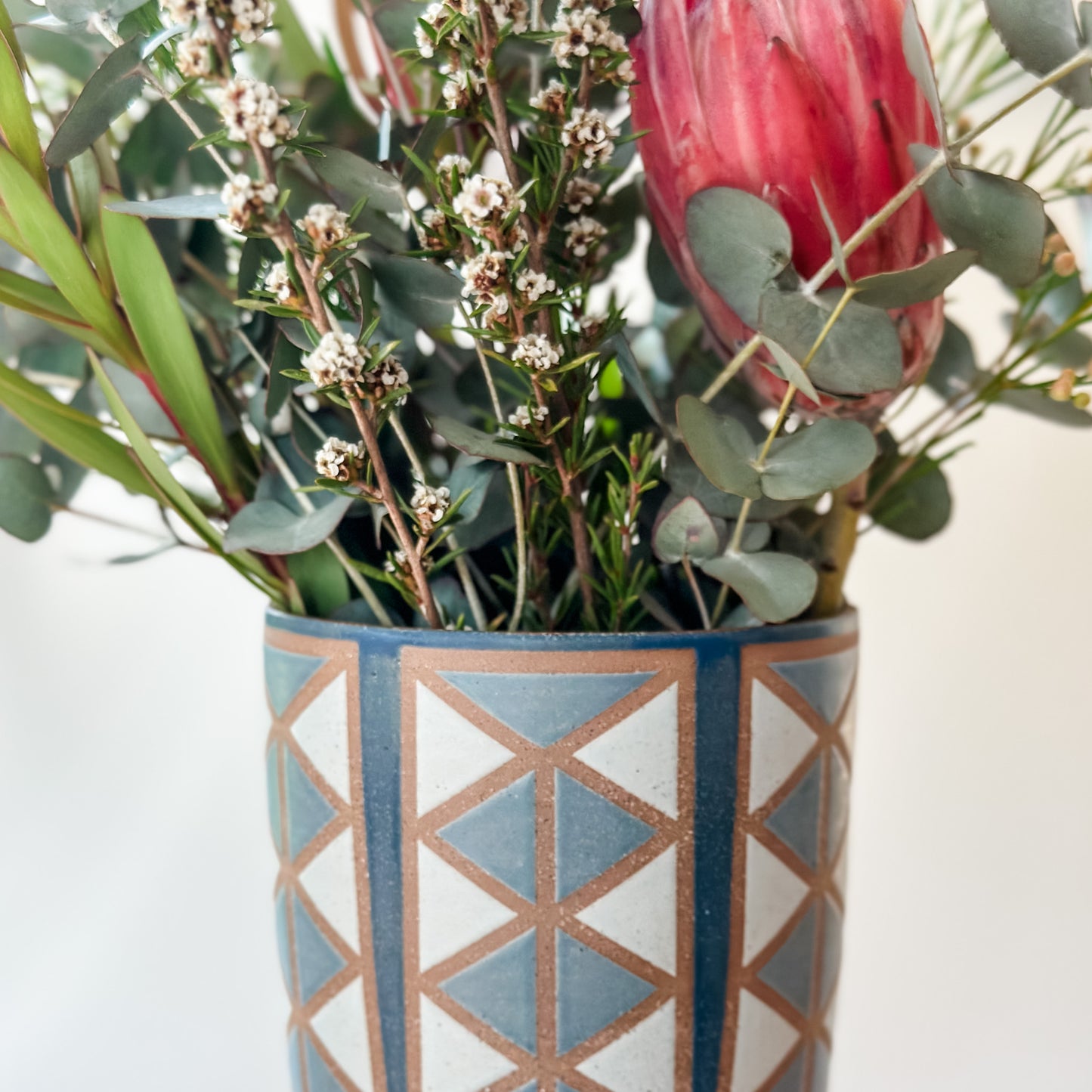 Decorative vase with geometric pattern filled with flowers on a light background