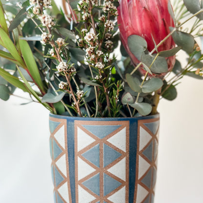Decorative vase with geometric pattern filled with flowers on a light background
