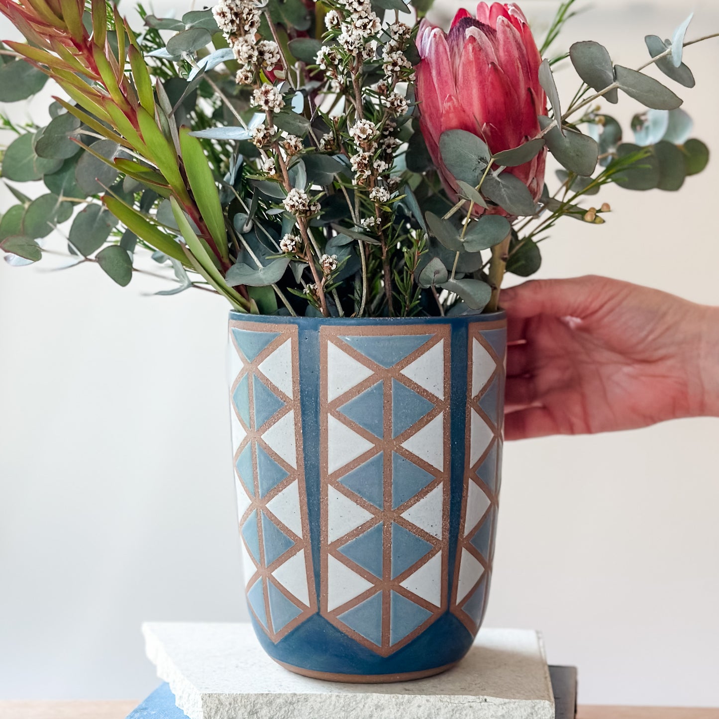 Hand holding a geometric-patterned vase with flowers against a white background