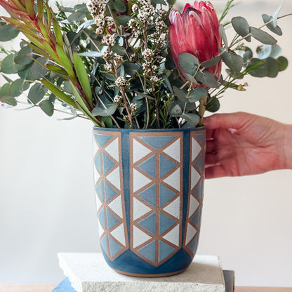 Hand holding a geometric-patterned vase with flowers against a white background