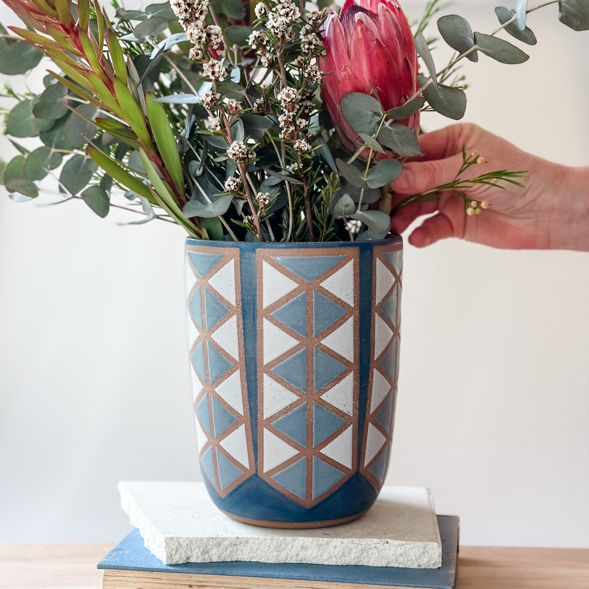 Person arranging flowers in a geometric-patterned vase on a white surface
