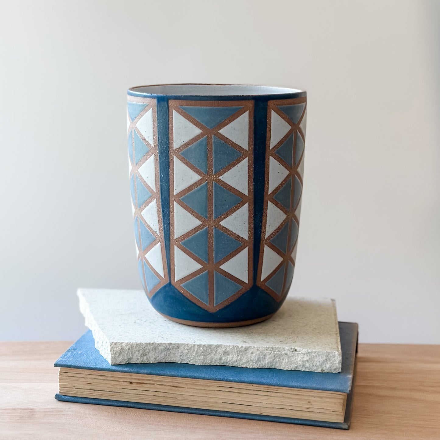 Ceramic vase with geometric pattern on a stack of tiles and books.