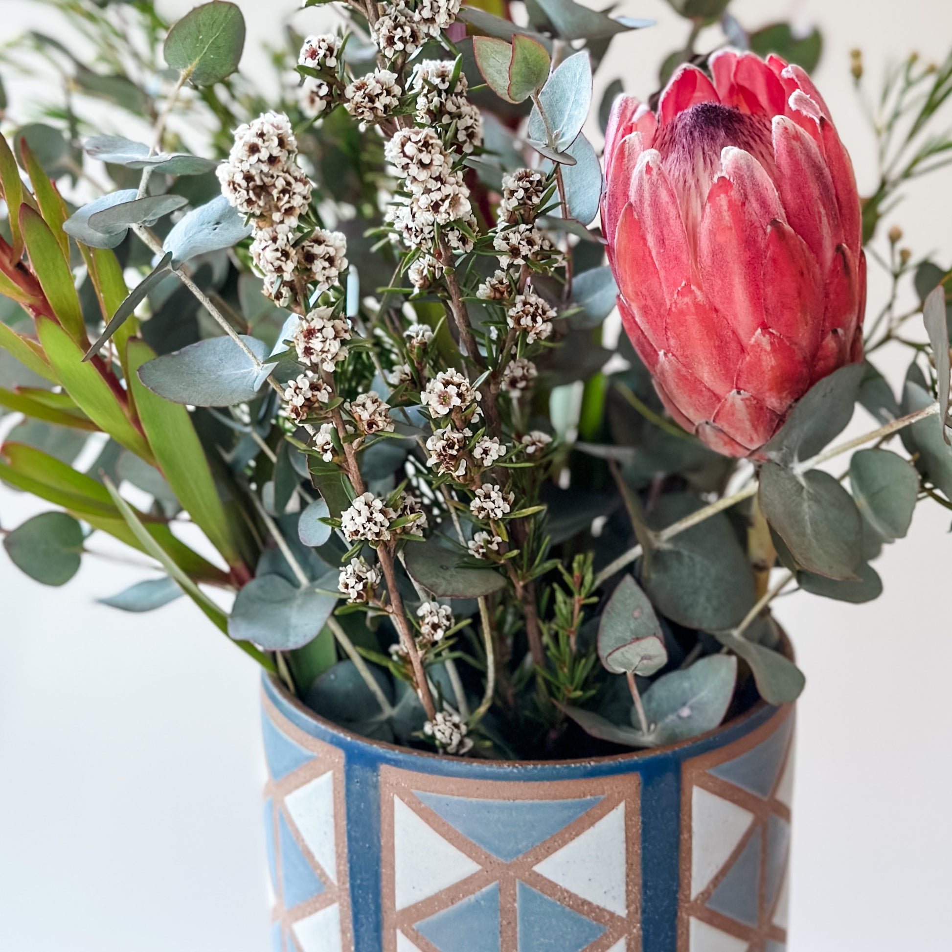 Floral arrangement with a pink protea in a geometric-patterned vase on a light background