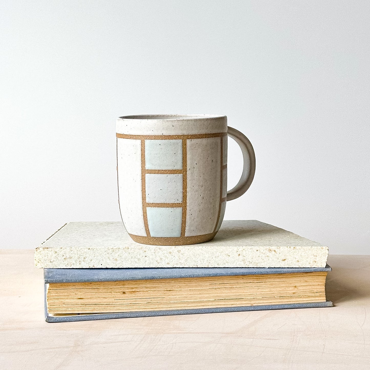 A view of a geometric styled mug on top of a tile and a book.