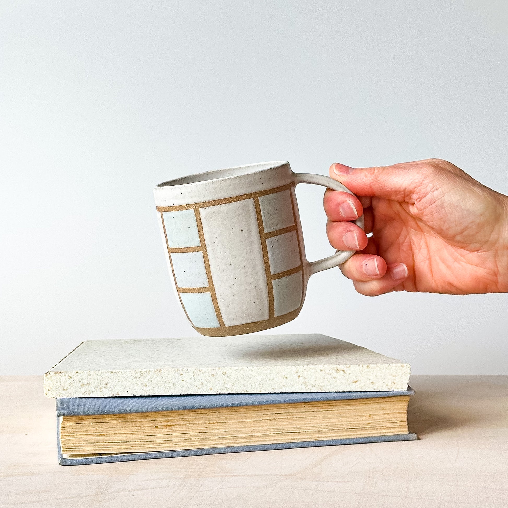 A hand holding a geometric styled mug above a tile.