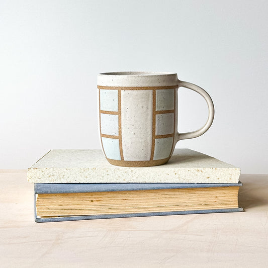 A geometric styled mug on a tile with a light background.