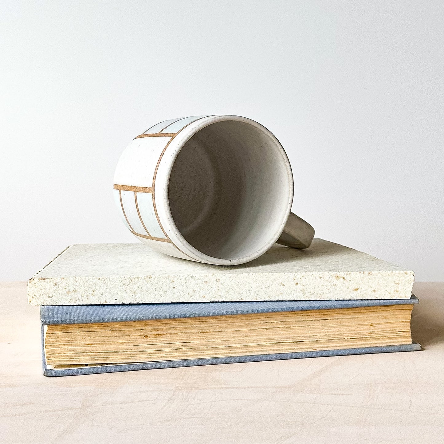 White mug with brown stripes on top of a book against a white background