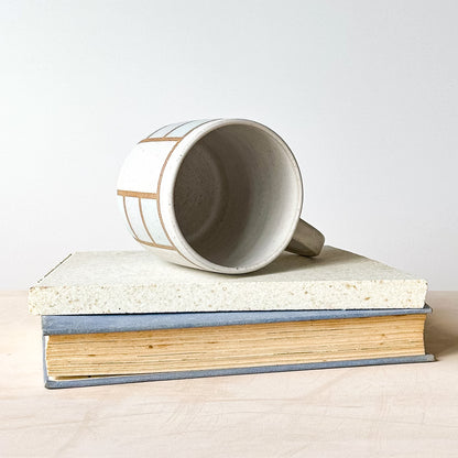 White mug with brown stripes on top of a book against a white background
