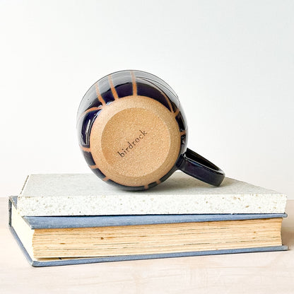 Navy mug with natural clay base on a stack of books, featuring 'birdrock' branding.