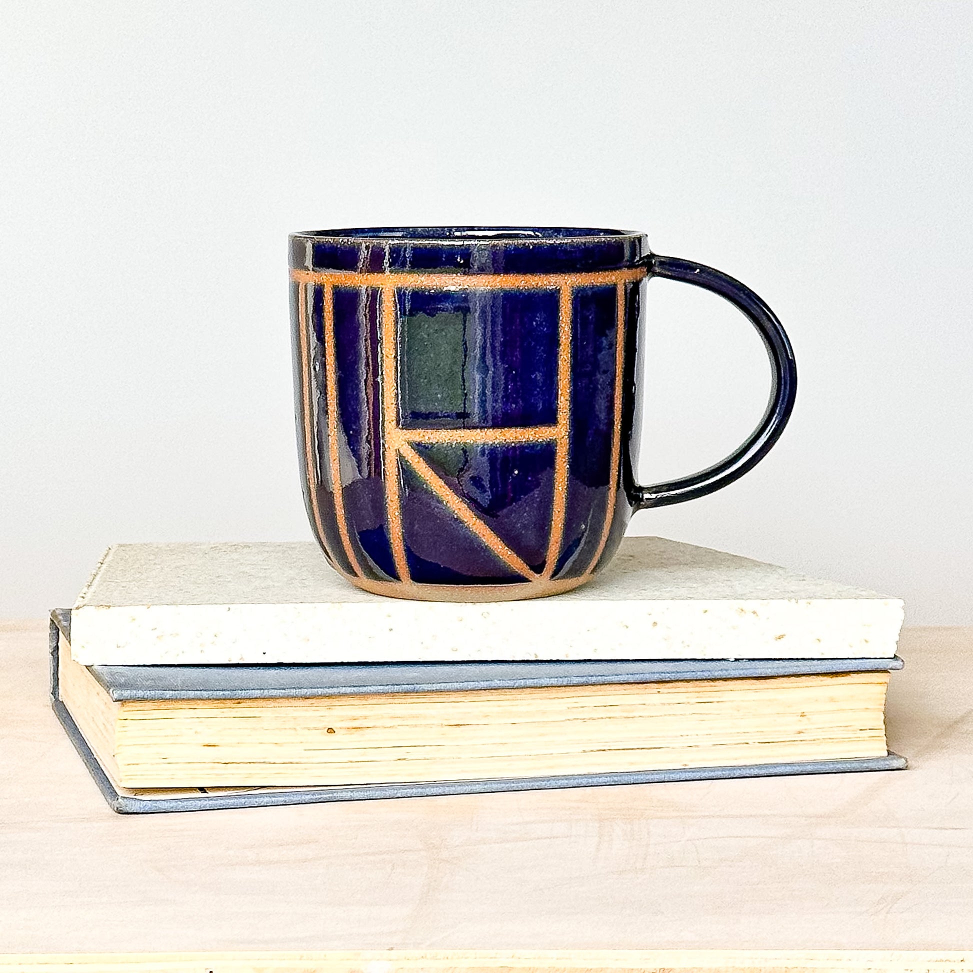 Navy blue ceramic mug with geometric pattern on a stack of books