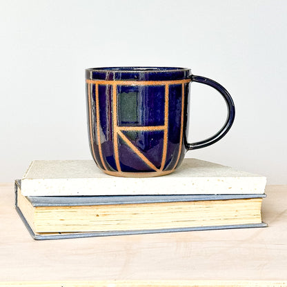 Navy blue ceramic mug with geometric pattern on a stack of books