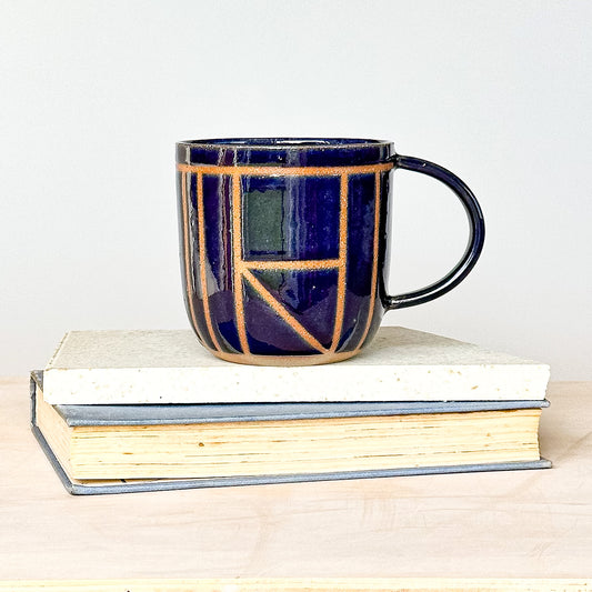 Navy blue ceramic mug with geometric pattern on a stack of books
