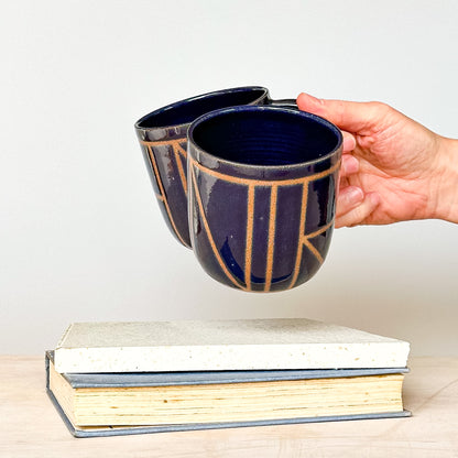 Person holding a blue ceramic mug with gold accents above a stack of books on a light background